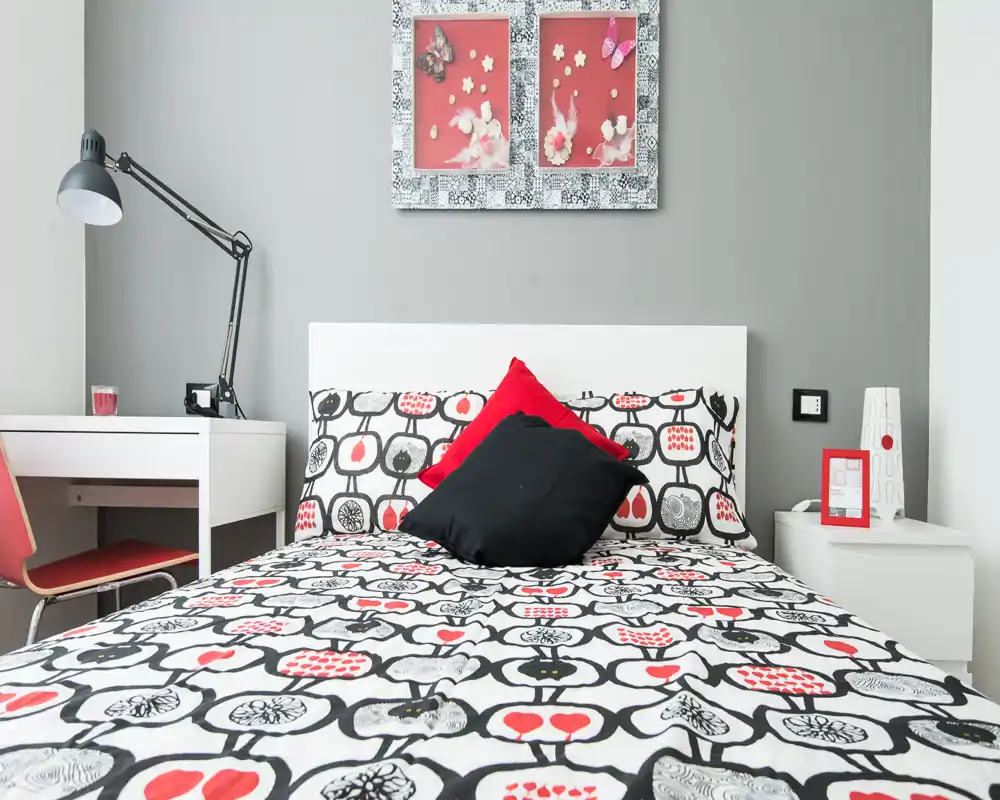 Bright, modern bedroom with patterned bedding and accent pillows, a white headboard and simple bedside tables — ideal for a stylish rental listing.