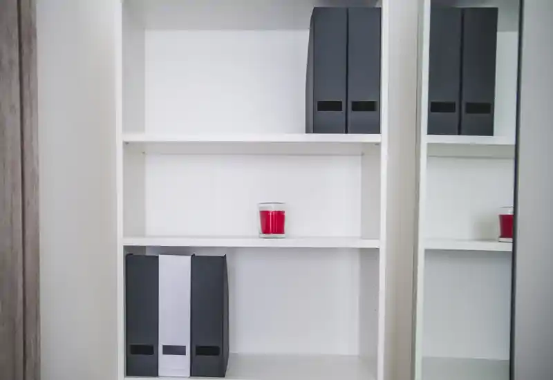 The image shows a close-up of white shelving with a few black binders and a red candle, plus a mirror reflecting part of the shelf. There are no visible features that clearly indicate a bedroom, living room, kitchen, bathroom, entrance, outdoor space, or dining area.