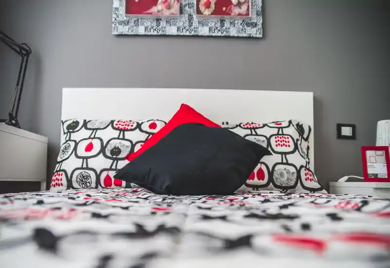 Bright, modern bedroom with patterned bedding and decorative cushions; a white headboard, bedside tables and coordinated wall art create a stylish, welcoming atmosphere.