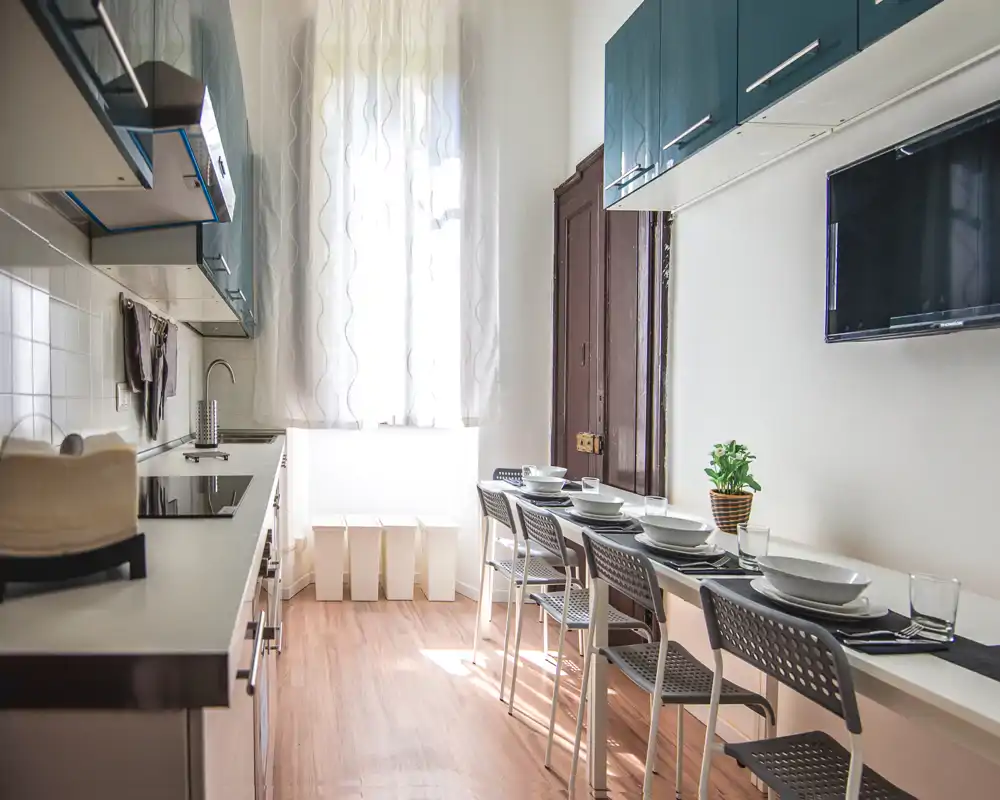 Cocina moderna y luminosa con una larga barra-comedor preparada para varios comensales. La luz natural inunda el espacio y los muebles contemporáneos crean un ambiente limpio y acogedor.