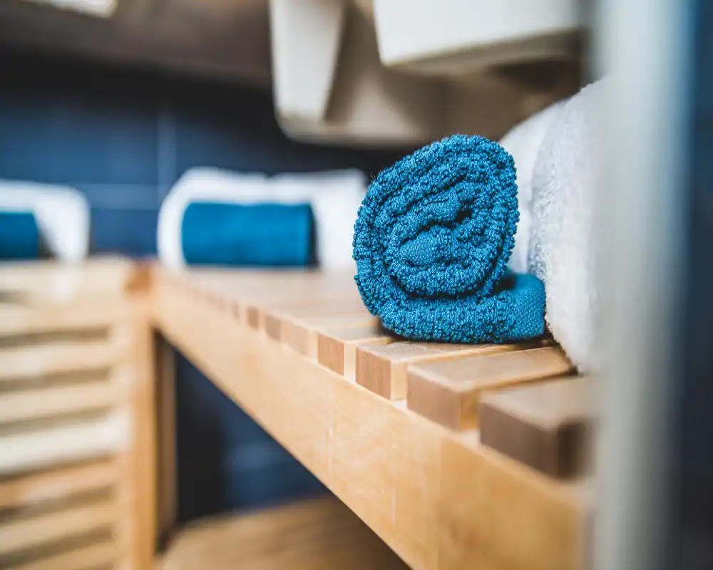 Primer plano de toallas enrolladas ordenadamente sobre un banco de madera, que sugiere un baño o zona de spa con ropa de cama limpia y bien presentada.