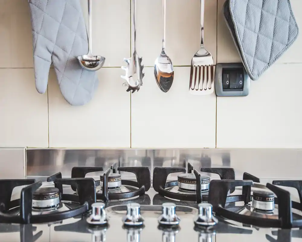 Primer plano de una encimera de gas moderna con utensilios colgados y manoplas, mostrando una zona de cocina limpia y ordenada, perfecta para fotos culinarias y anuncios centrados en electrodomésticos.