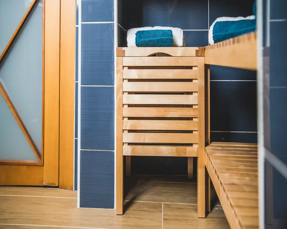 Rincón de baño ordenado con banco de madera y cajón de almacenamiento, toallas dobladas encima y azulejos azul oscuro, acabado moderno estilo spa.