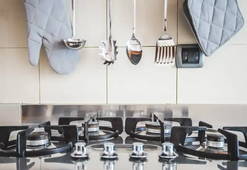 Primo piano di un piano cottura moderno con quattro fuochi a gas, superfici in acciaio inox e utensili appesi — un'area di cottura pulita e funzionale ideale per annunci.