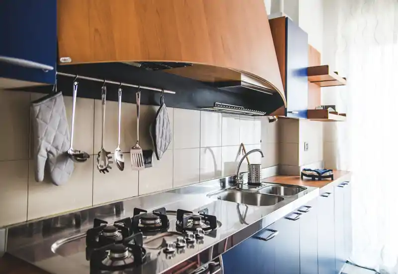 Cucina moderna con piano in acciaio inox, piano cottura a gas e lavello doppio; mobili in legno caldo e utensili appesi creano un'area cucina pratica e attraente.