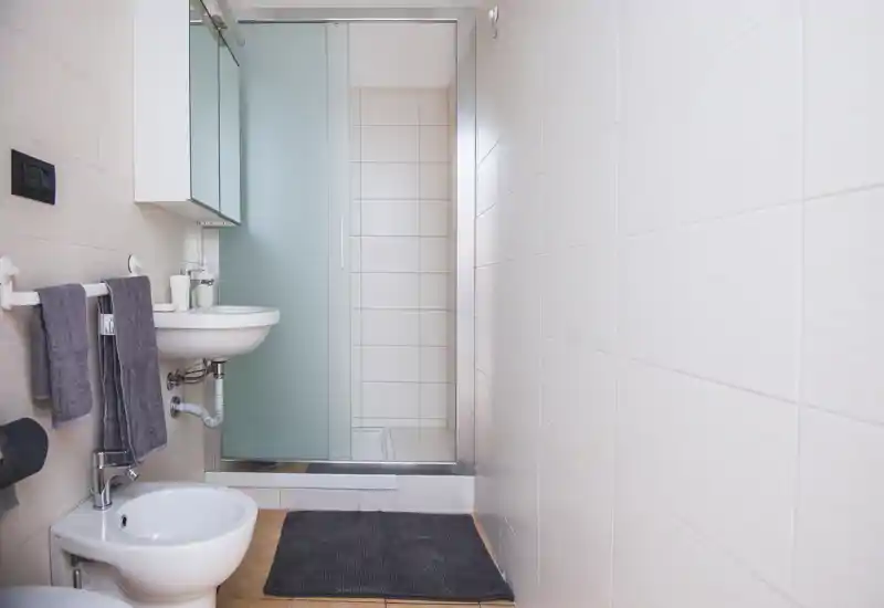 Clean, modern bathroom with wall-mounted sink, bidet, glass shower door and neutral tiled walls; minimal, bright and functional.