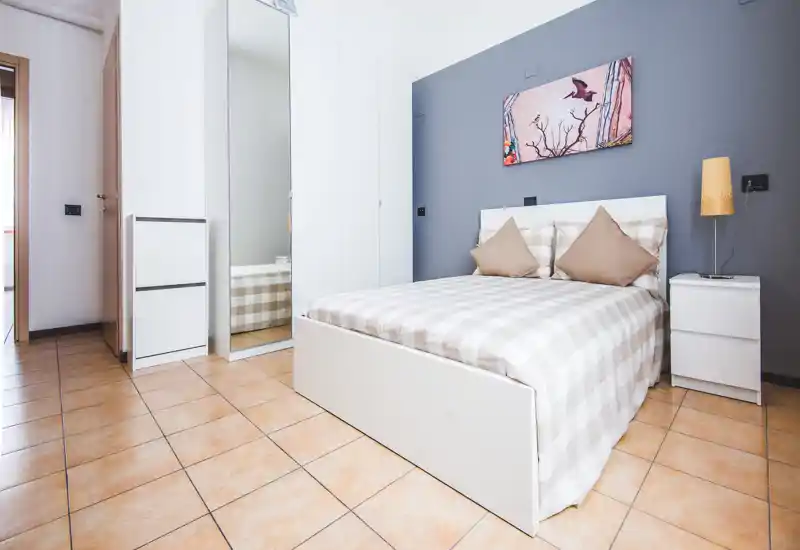 Modern, neatly staged bedroom with a double bed, neutral checked bedding, bedside tables and a wardrobe with mirrored door; soft lighting and calm grey accent wall create a cosy atmosphere ideal for rental photos.