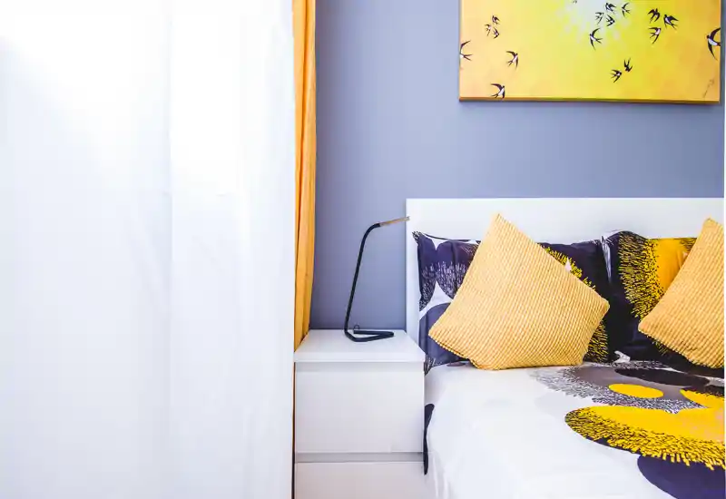 Bright, modern bedroom corner with coordinated yellow accents, cushions and a bedside table with a slim lamp — clean, inviting styling ideal for listings.