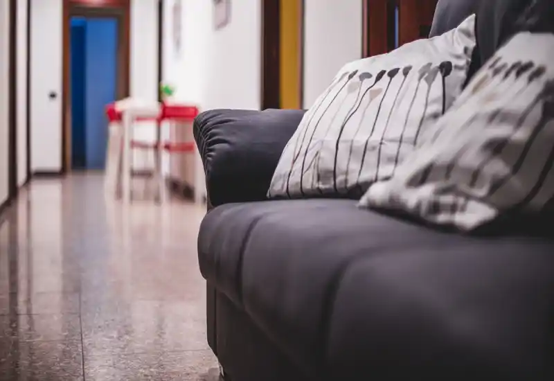 Close-up of a soft sofa in a living area with patterned cushions and a long hallway in the background; warm, intimate composition suitable for a rental listing highlighting lounge comfort.