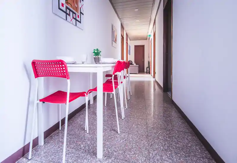 Narrow dining area with a slim white table and a row of bright red chairs along a hallway; modern, space-saving setup ideal for compact apartments.
