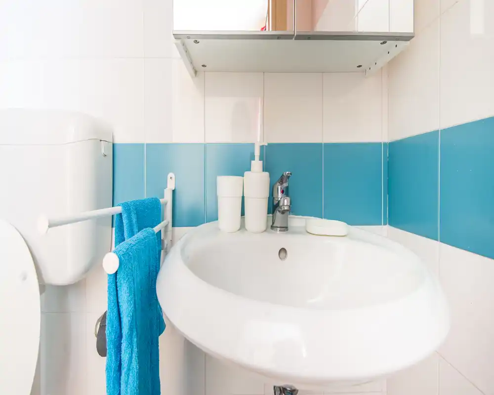 Bright, clean bathroom sink with modern faucet, soap dispenser and matching blue towel—compact and well maintained.