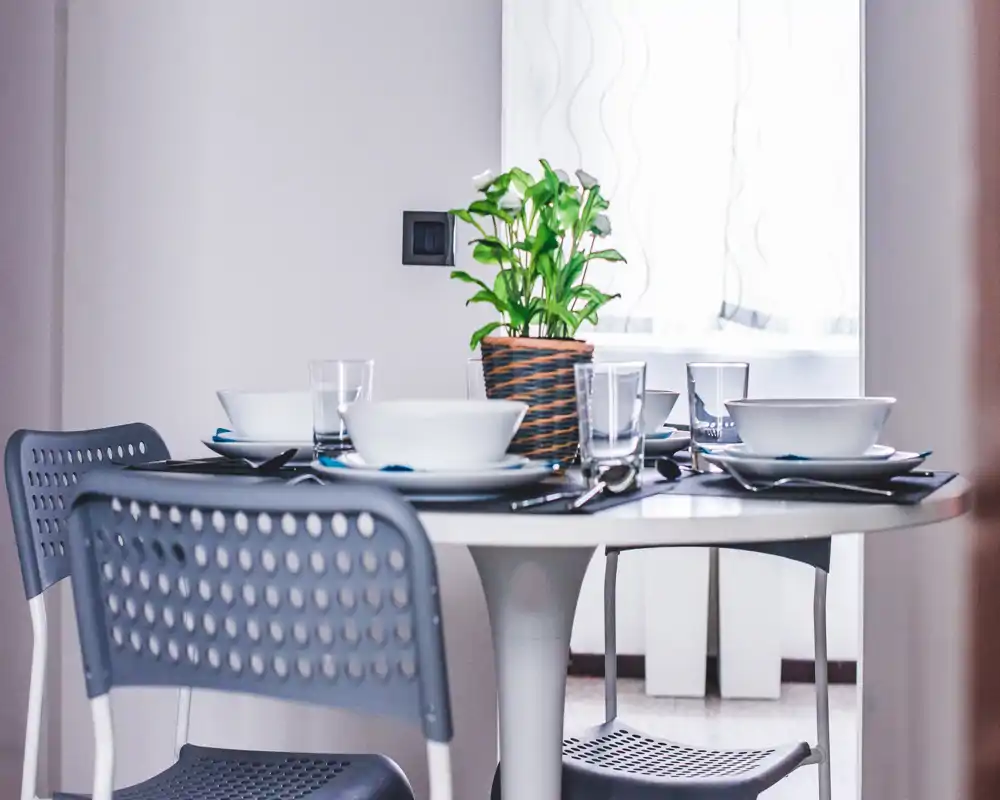 Bright, modern dining area with a round table set for four, contemporary perforated chairs and a potted plant centerpiece.