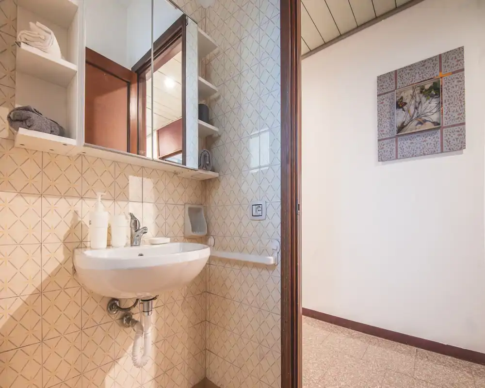 Compact, well-lit bathroom with a wall-mounted sink, mirror cabinet and tiled walls. Clean and functional space ideal for short stays.