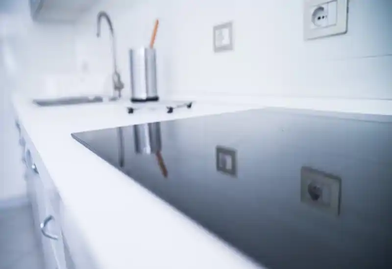 Minimal modern kitchen counter with an induction cooktop and stainless utensil holder; bright white surfaces and a sleek, uncluttered look.