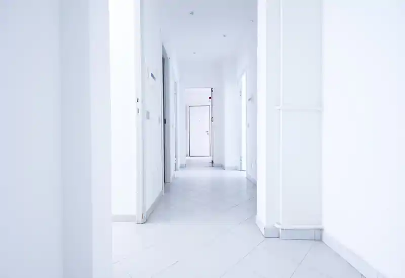 Bright, minimal hallway/entrance with white walls, tiled floor and a door at the end; clean, modern and well-lit space suitable for an apartment entry.