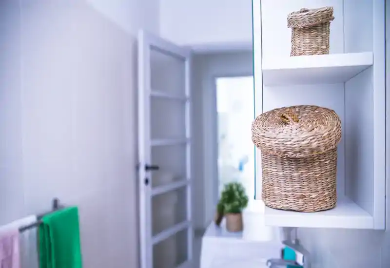 Compact, well-lit bathroom shelf with woven storage baskets and a sink; towels and a towel rail visible, giving a tidy, styled appearance.