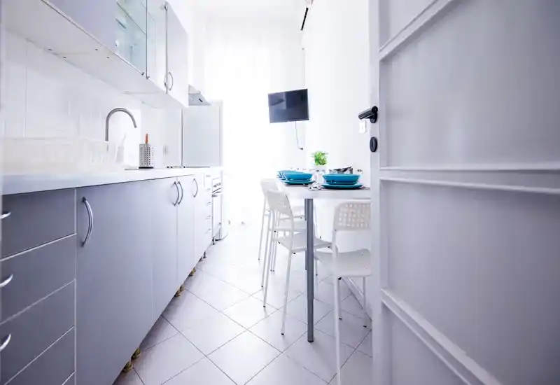 Bright modern kitchenette with sleek cabinetry, a small dining table set for four and a wall-mounted TV — ideal for compact urban stays.
