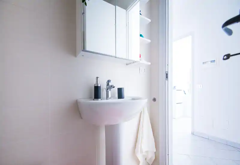 Bright, modern bathroom with a pedestal sink, mirrored cabinet and soft beige tiles; clean minimalist styling and good natural light.