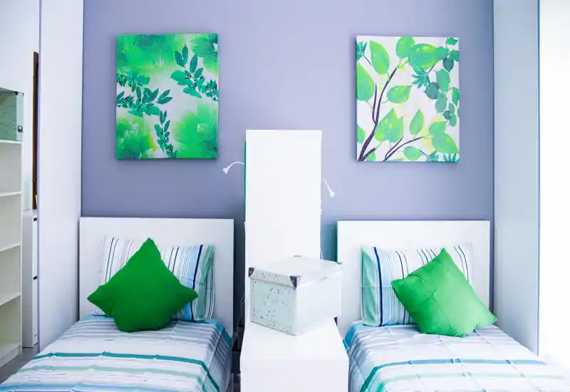 Dormitorio luminoso y moderno con dos camas individuales, cojines verdes y cuadros botánicos a juego — ideal para huéspedes o habitación compartida.