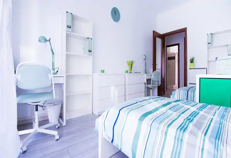 Dormitorio doble luminoso y moderno con ropa de cama a rayas, dos escritorios y estanterías: bien iluminado y preparado para anuncios de alquiler.