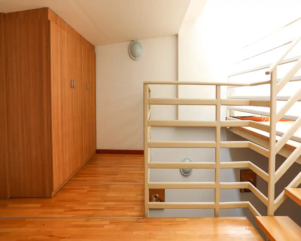 Landing/entrance area with wooden flooring, built-in wardrobes and a railing overlooking a staircase; bright natural light from the right.
