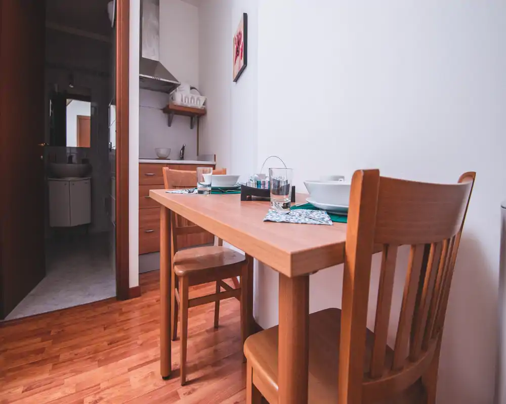 Pequeña zona de comedor con mesa de madera para dos. Estilo sencillo y acogedor, luz natural y servicio coordinado, ideal para un apartamento pequeño.