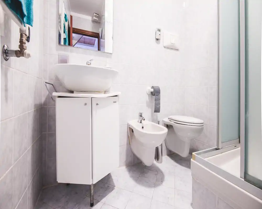 Baño pequeño y luminoso con lavabo sobre mueble, bidé, inodoro suspendido y cabina de ducha; azulejos claros y sanitarios nítidos que ofrecen un espacio funcional y limpio.