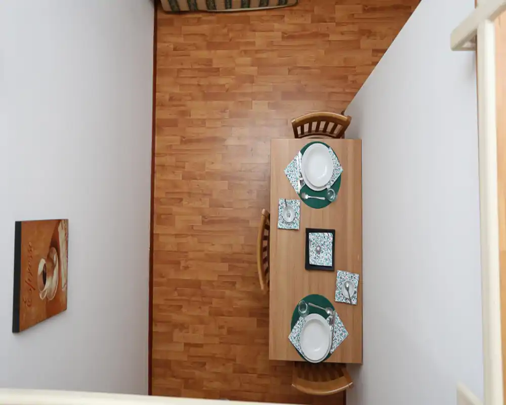 Vue plongeante d'une table à manger dressée pour deux sur un sol en bois ; espace simple, bien éclairé avec sets et vaisselle assortis.