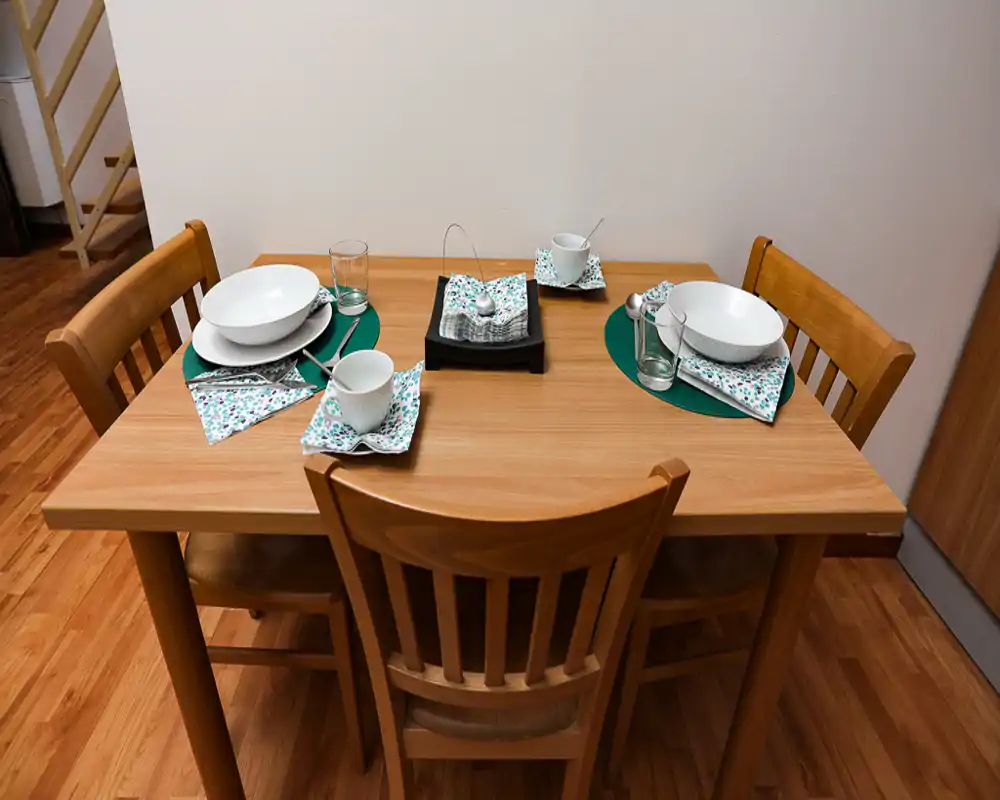 Table à manger en bois dressée pour trois personnes avec chaises assorties, sets de table et vaisselle disposée proprement — idéale pour des annonces d'appartements mettant en valeur un coin repas cosy.