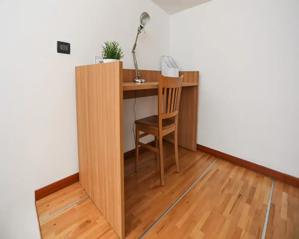 Bureau en bois simple et chaise contre un mur blanc dans un coin de la pièce, décoré d'une lampe et d'une petite plante — parfait pour un coin bureau compact en chambre.