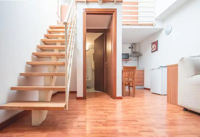 Espace de vie lumineux et soigné avec parquet, escalier ouvert et coin repas/cuisine visible — idéal pour un loft ou studio compact.