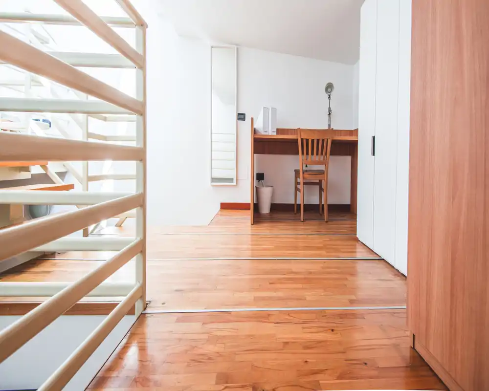 Bright minimal loft area with wooden floors, a small desk and chair by the wall — ideal as a compact workspace within a living space.