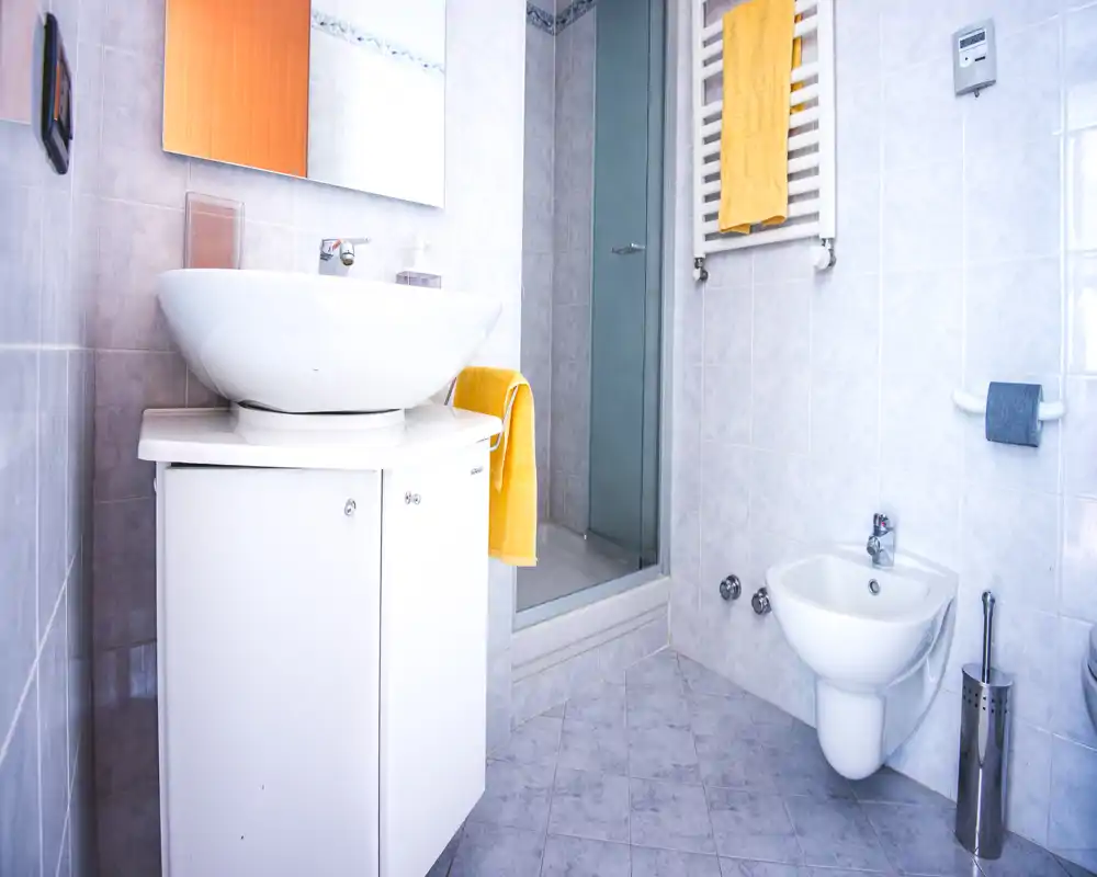 Bright, compact bathroom with a modern washbasin, bidet and a shower cubicle; light tiles and yellow towels add a fresh touch.