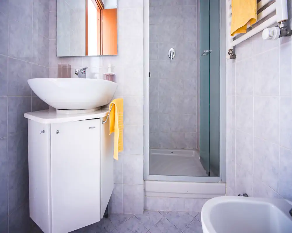 Compact, clean bathroom with a modern vessel sink, shower cubicle and wall-mounted radiator with towels — bright, tiled space ideal for short stays.
