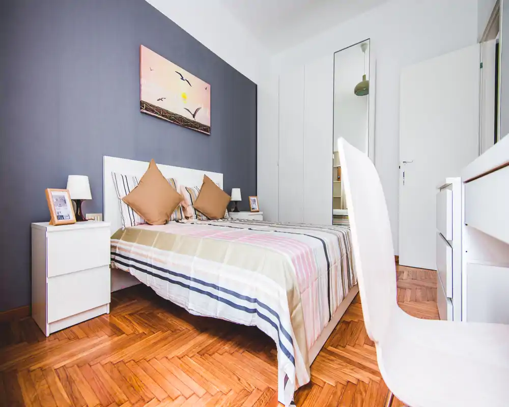 Camera da letto moderna e luminosa con letto matrimoniale, biancheria coordinata e comodini. Stile pulito, pavimento in parquet e armadio con specchio rendono l'ambiente accogliente.