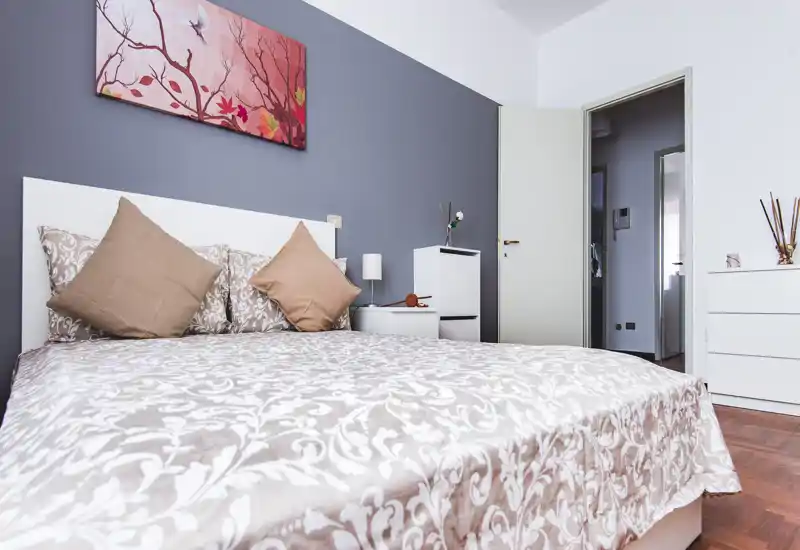 Dormitorio luminoso y bien preparado con una amplia cama estampada, cojines neutros y cuadro decorativo — ideal para una estancia relajante.