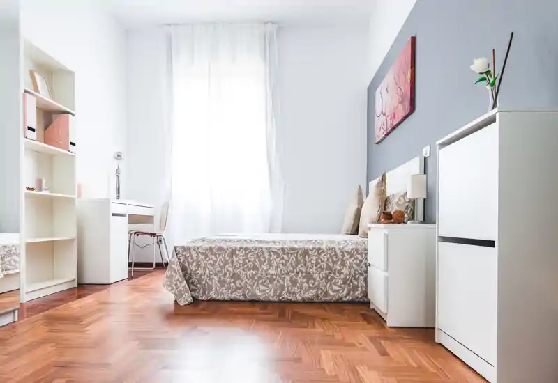 Dormitorio luminoso y bien presentado con colcha con estampado, mesitas de noche y luz natural de una gran ventana — decoración minimalista y suelo de parquet cálido que crean un ambiente acogedor.