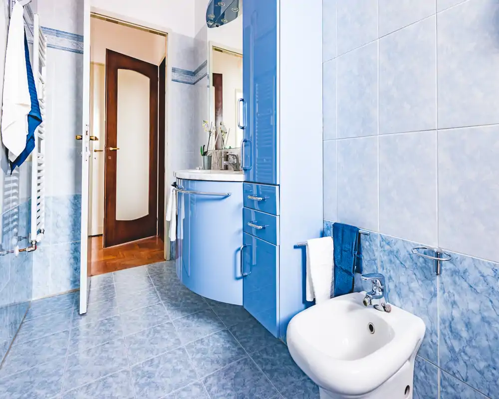 Bagno moderno e luminoso con piastrelle azzurre, bidet e lavabo con mobile sottostante. Spazio pulito e ben illuminato, ideale per foto dell'annuncio.
