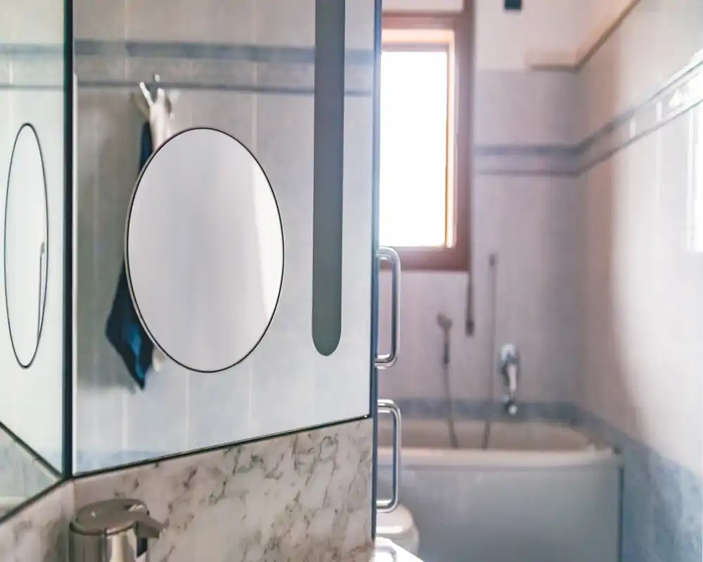 Bagno moderno ben illuminato con pareti piastrellate, vasca e pensile con specchio; tonalità neutre e luce naturale da una finestra.