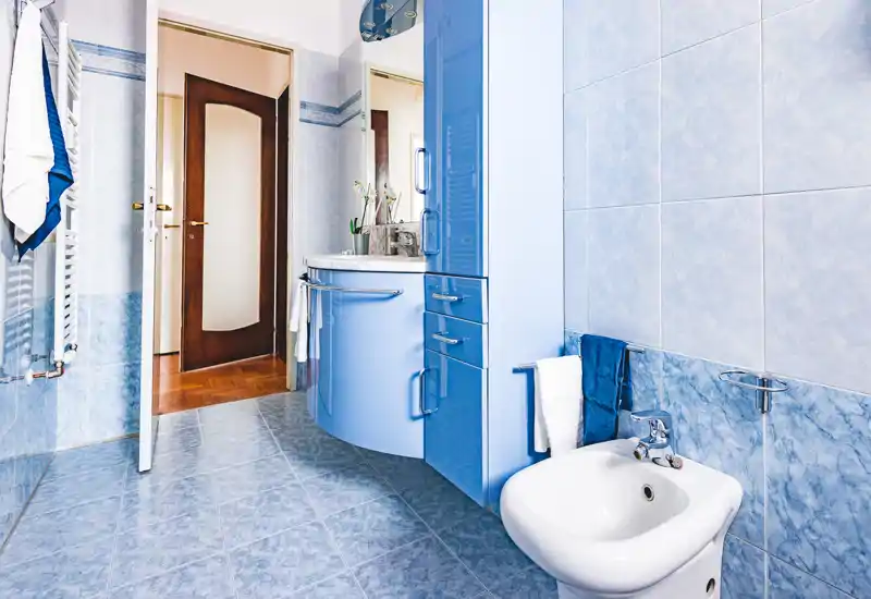 Bagno luminoso e ben curato con piastrelle blu, bidet e mobile lavabo curvo con specchio e spazio contenitivo — pulito e accogliente.