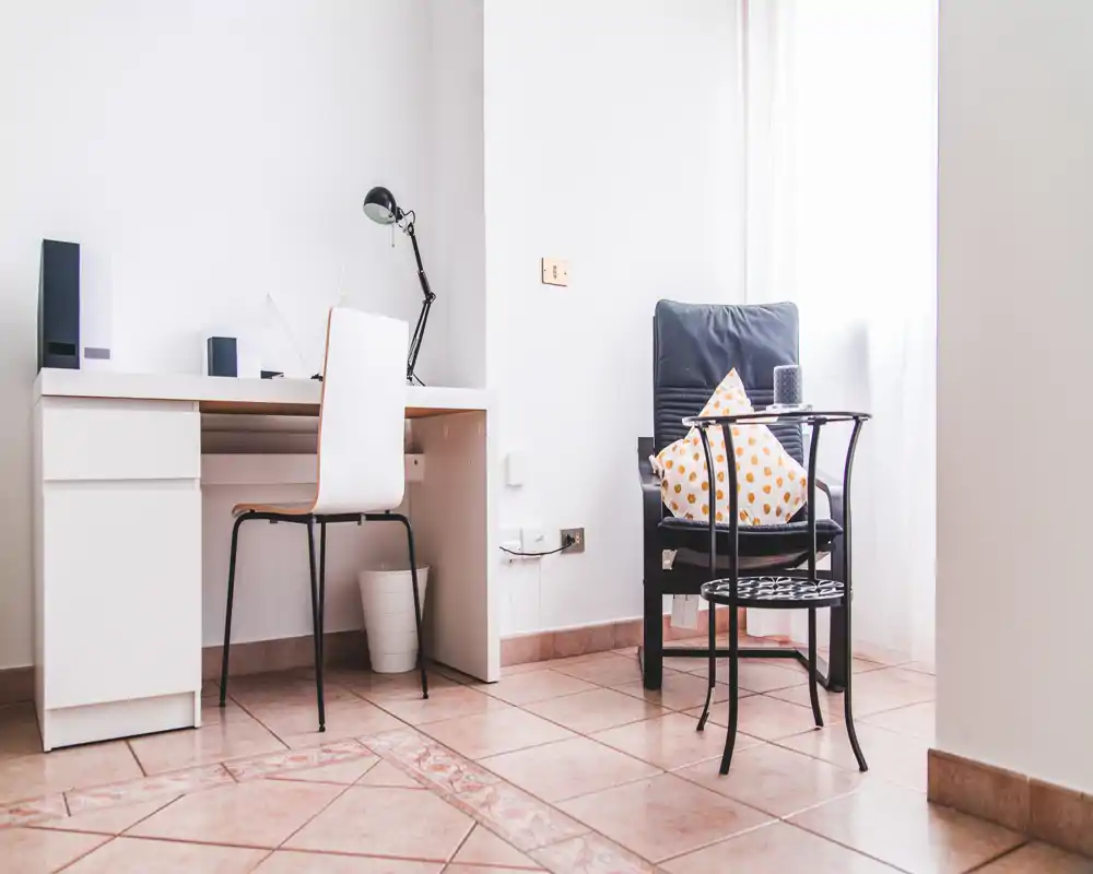 Angolo soggiorno luminoso e minimale con poltrona comoda, tavolino e una piccola scrivania — ideale per rilassarsi o lavorare vicino alla finestra.