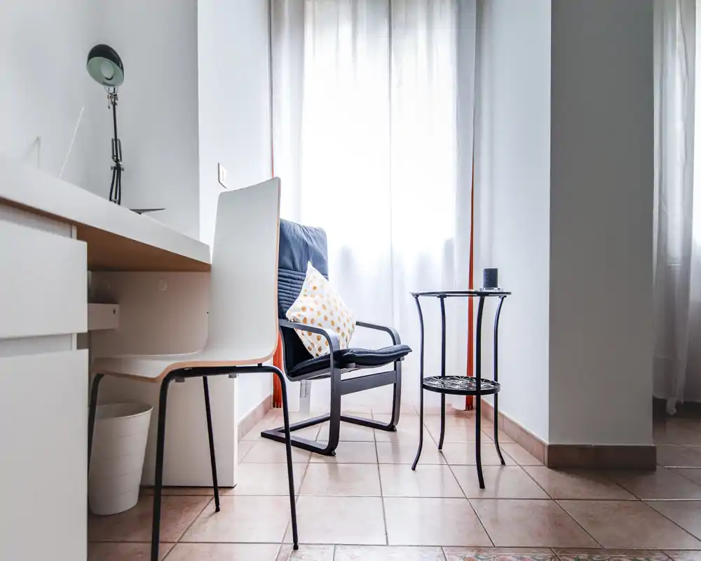 Angolo giorno luminoso e minimalista con una poltrona comoda, un tavolino e una sedia da scrivania vicino a una finestra luminosa — ideale per leggere o lavorare.