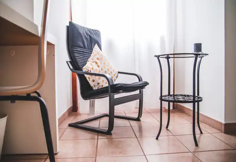A bright, minimalist living corner with a modern black armchair and side table beside a sheer-curtained window; ideal for a quiet reading nook.