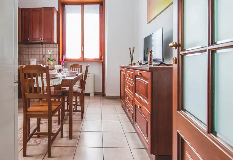 Bright, cozy dining area with a wooden table and chairs set beside an open kitchenette and a window providing natural light.