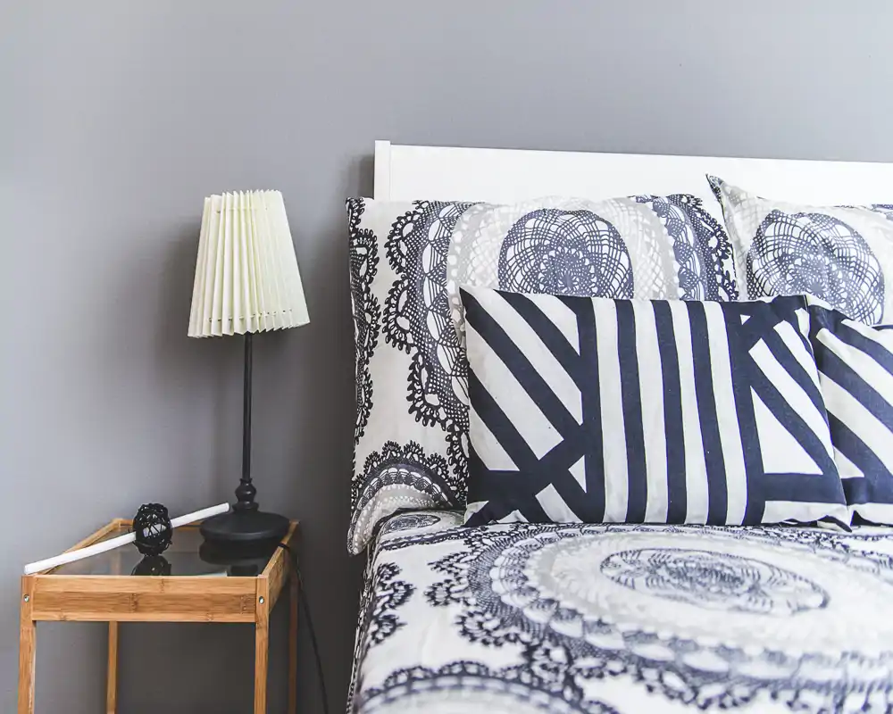 Bright, modern bedroom corner with patterned bedding, decorative cushions and a bedside table with a lamp — a cozy, well-styled spot ideal for rental photos.