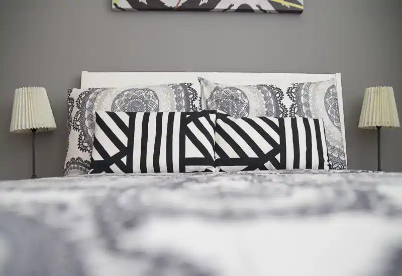 Stylish bedroom close-up with patterned bedding, decorative pillows and balanced bedside lamps creating a cozy, modern atmosphere.