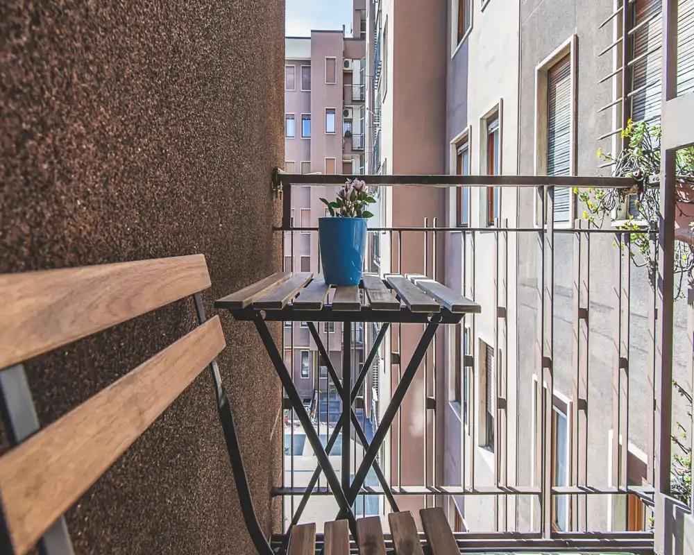 Cozy narrow balcony with a small wooden bistro table and chair, decorated with a potted plant — perfect for morning coffee in the city.