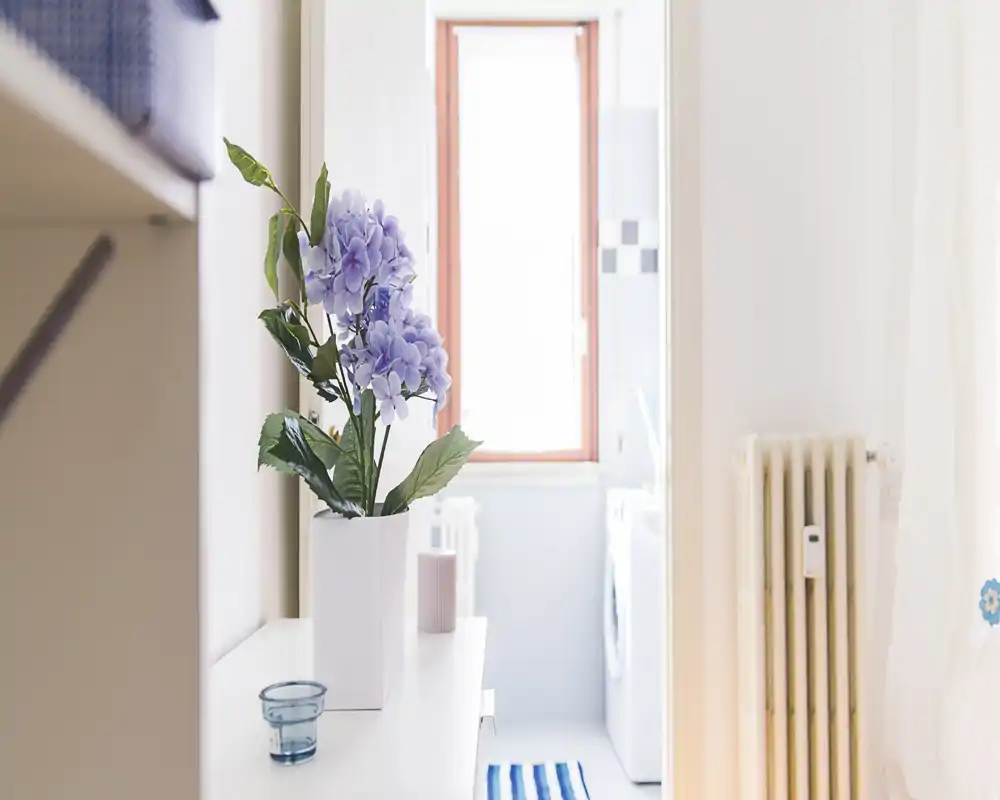 Bright, tidy entrance/hallway area with decorative flowers on a console table and a glimpse into a utility/bath area; soft natural light creates a welcoming first impression.
