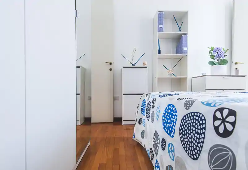 Bright, modern bedroom with patterned bedding, white storage units and wooden flooring — clean lines and soft decorative accents create a fresh, welcoming space.