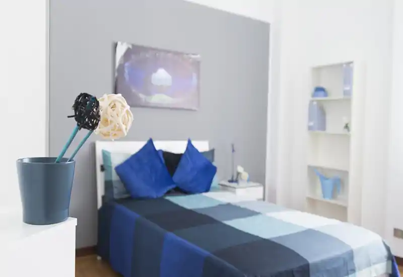 Bright, modern bedroom with a double bed dressed in blue patchwork bedding, decorative cushions and bedside table; soft daylight and coordinated decor create a welcoming atmosphere.